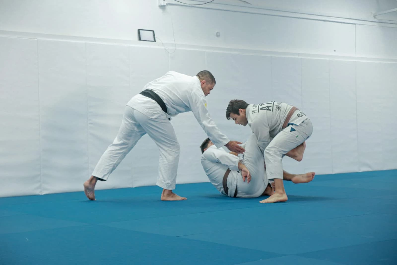 Three gi-clad practitioners working through a jiu-jitsu demonstration