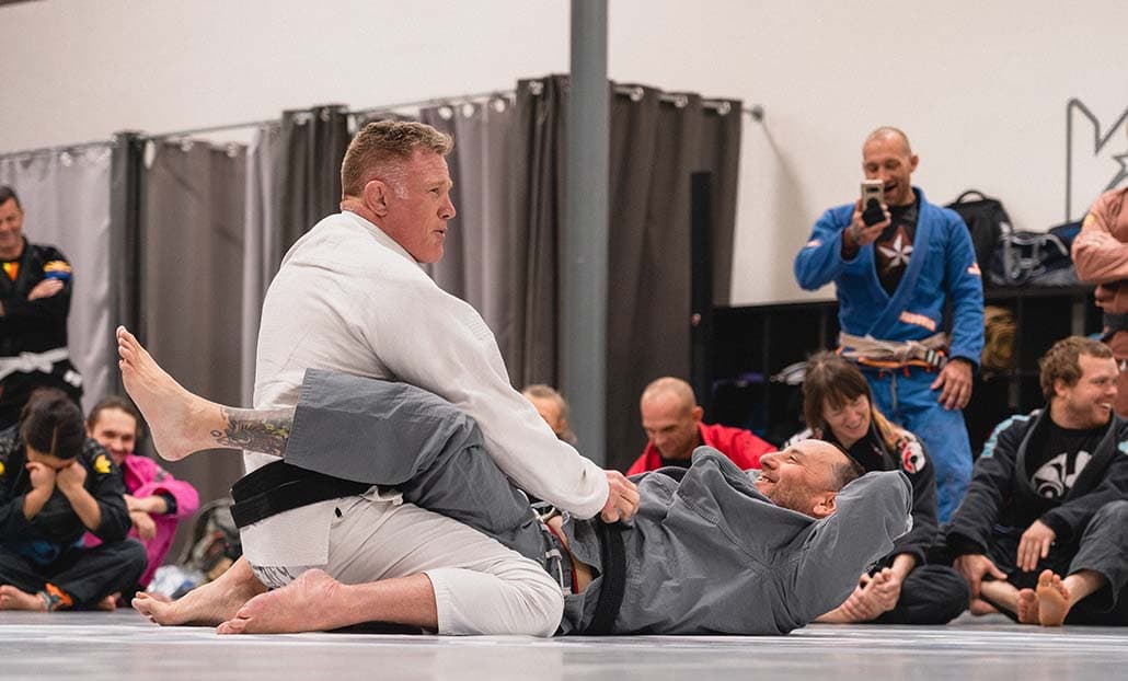 Students observing a gi technique demonstration on the mat.