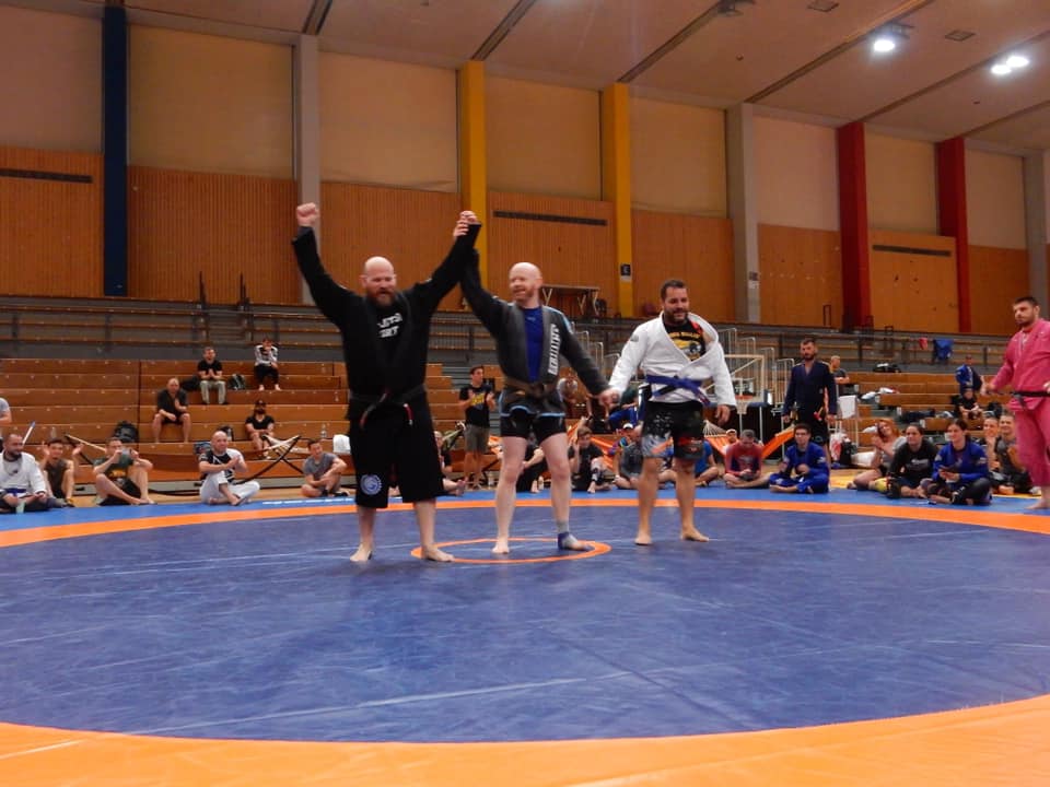 A referee standing between two no-gi competitors