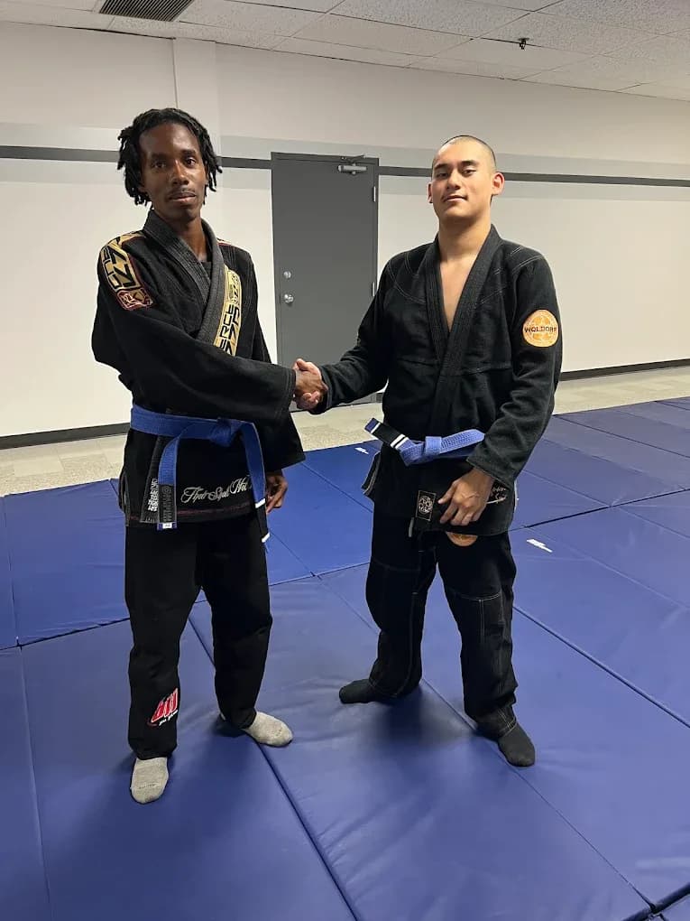 Two people in Brazilian Jiu-Jitsu gis shaking hands on blue mats inside Gracie Underground Brazilian Jiu Jitsu And Self Defense gym in Carpentersville, IL.