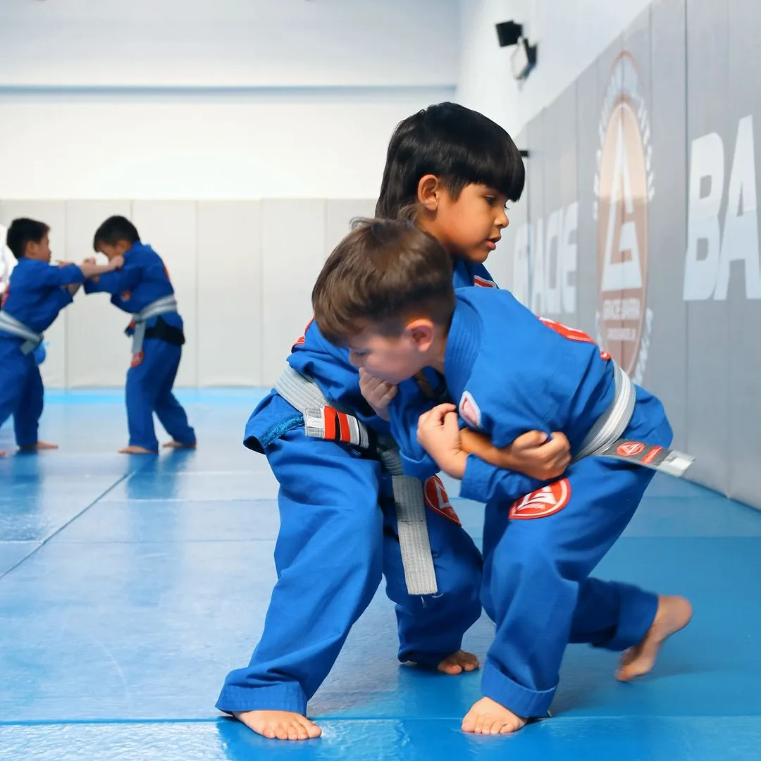 Children in blue gis practicing grappling on a gym mat during class