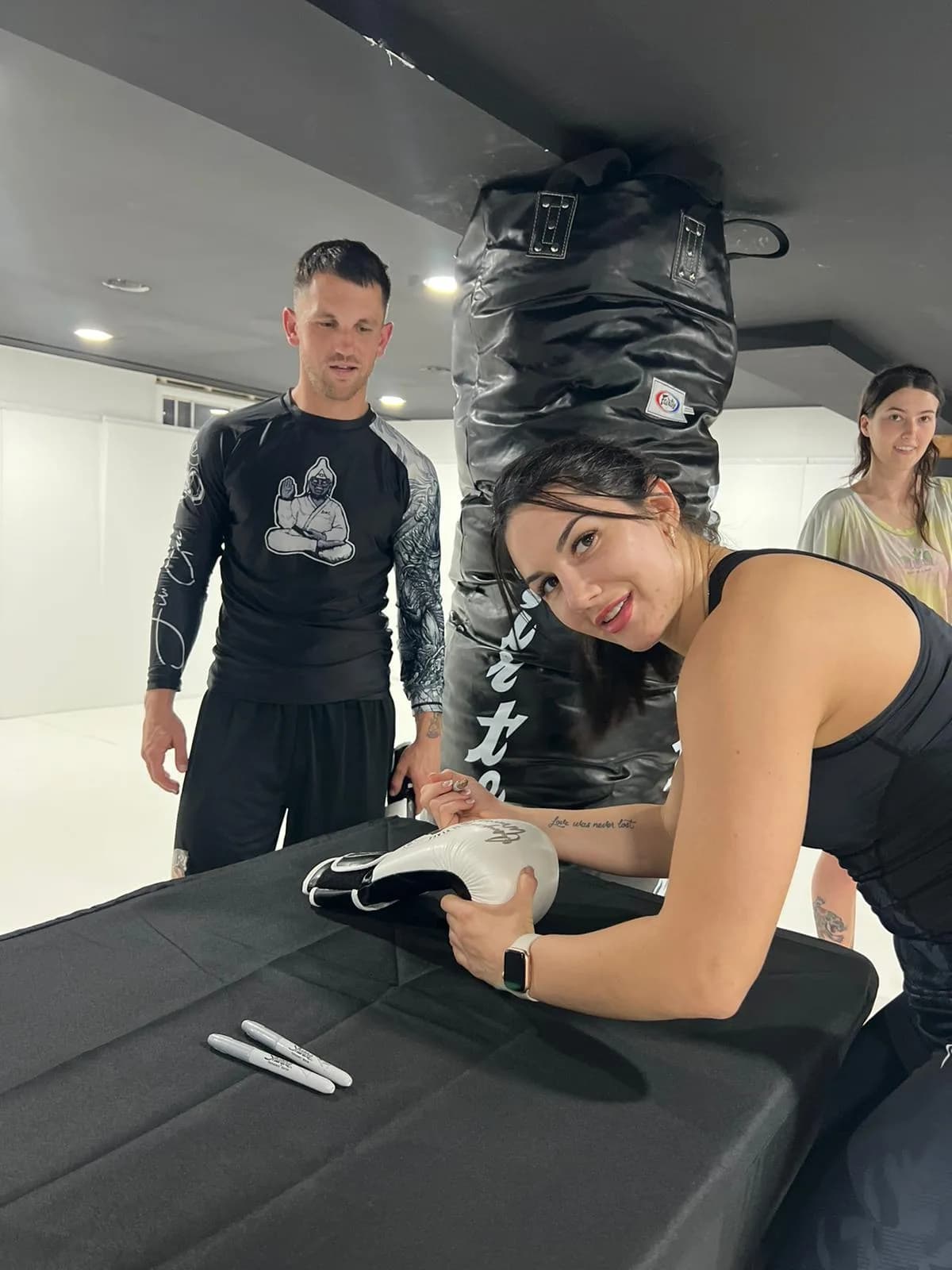 Place of Peace Brazilian Jiu Jitsu gym in Riverton, NJ, featuring a woman signing gloves at a table with training equipment.